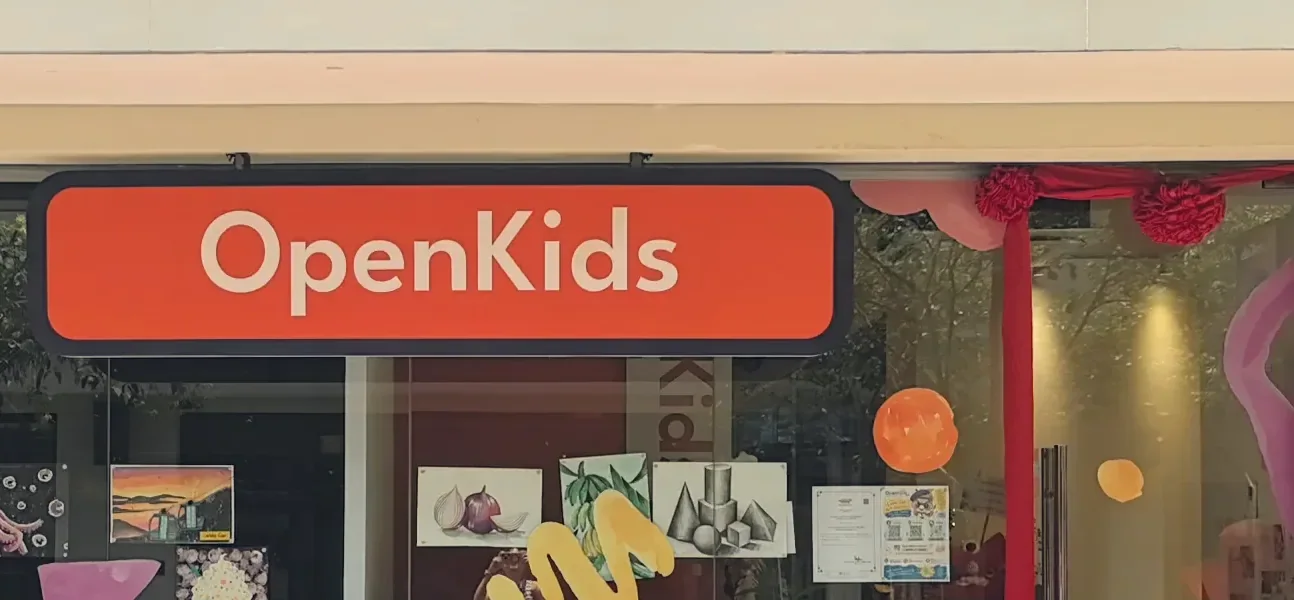 The orange OpenKids sign above the storefront of an OpenKids campus in Kuala Lumpur, with students' paintings in the window